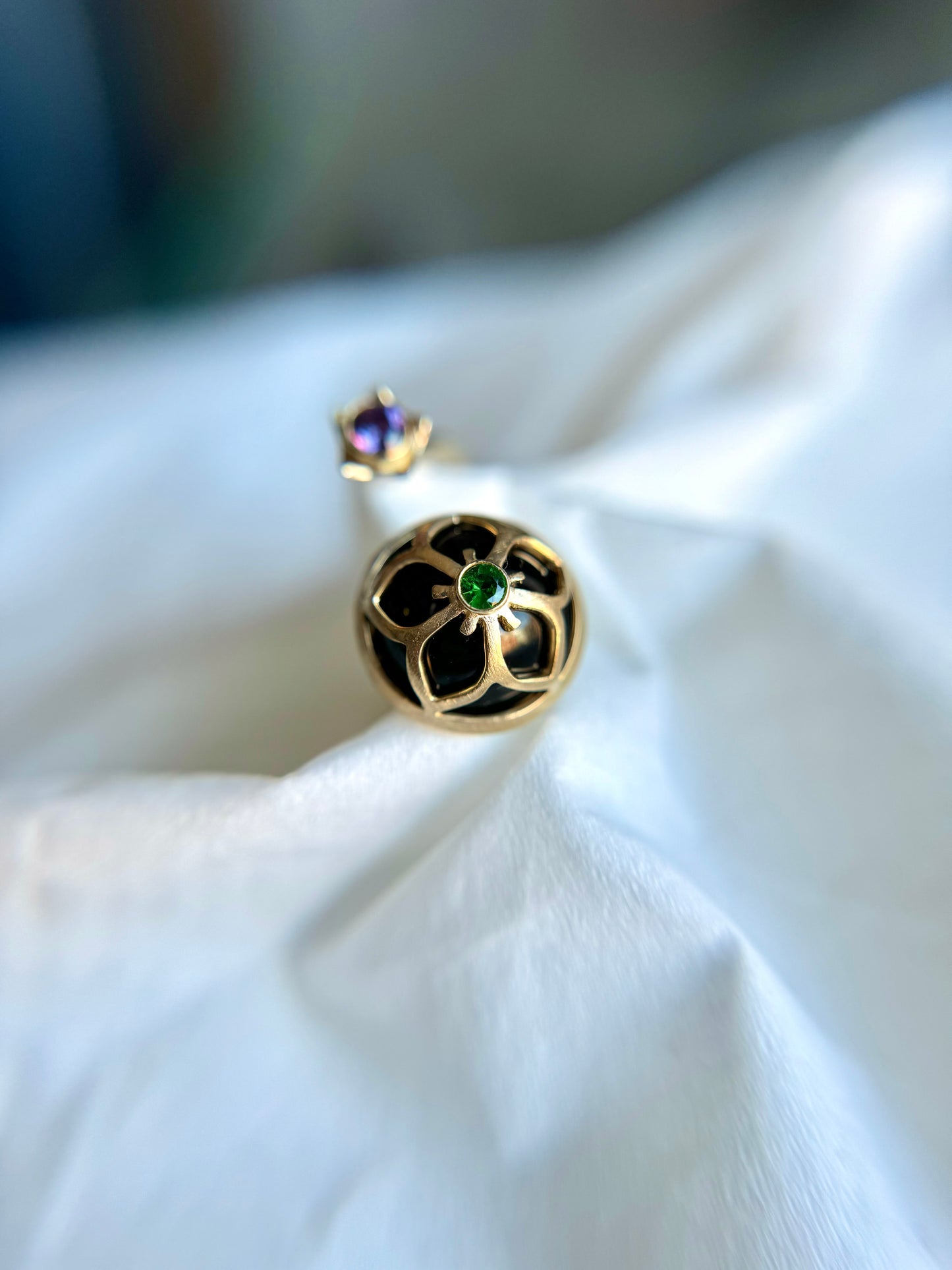 14 karat and 18 karat yellow gold bypass ring featuring a cutout balloon flower design with a tiny Tsavorite garnet on the top of dome shaped onyx. There is a 3mm purple sapphire on the other ring end