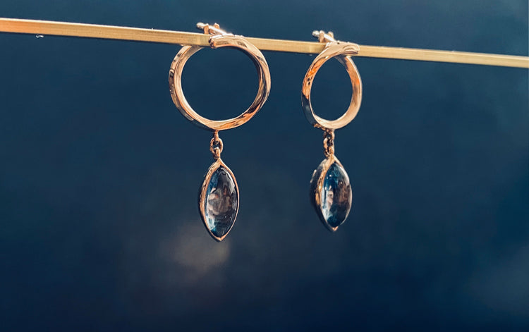 Gold hoop earrings with marquise shaped blue stones hanging on a gold bar with a blue background