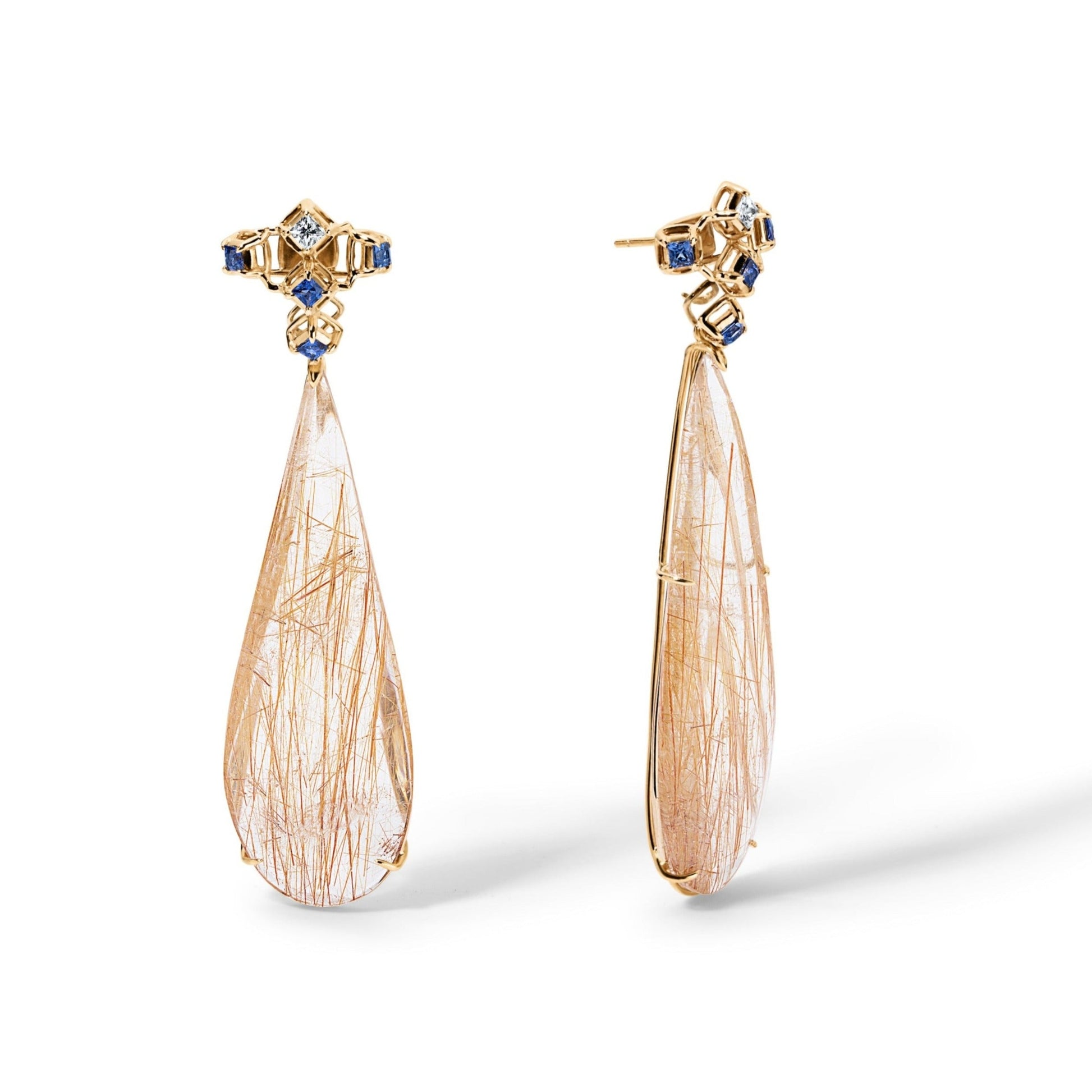 A pair of 14 karat yellow gold dangling earrings with Blue and White Sapphires. Its top part consists of five square cut, top is white and the others are blue sapphires. The bottom dangling part is tear drop shaped Rutilated Quartz. In the picture one is shown from the front and the other is diagonal. 